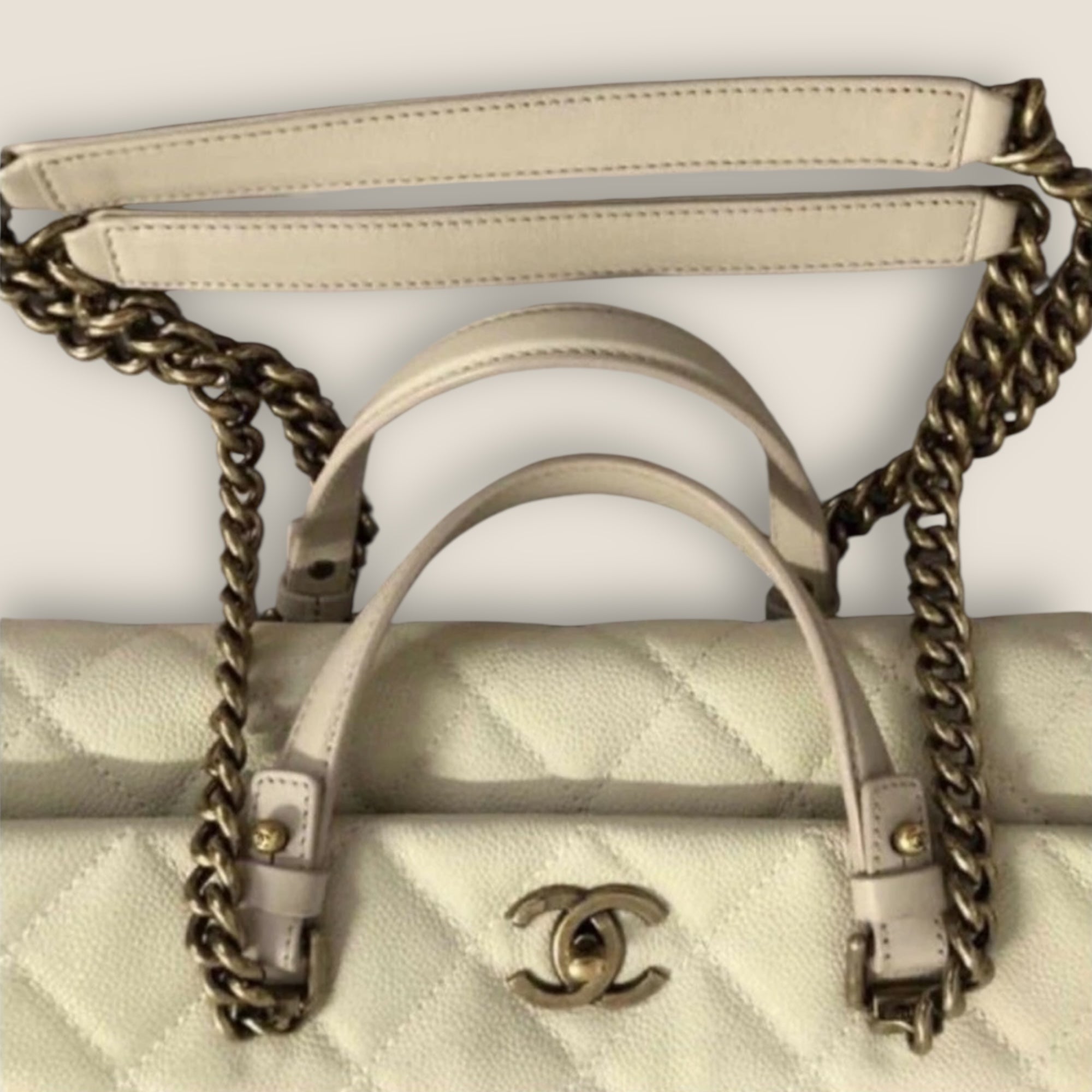 Close-up of a beige handbag with gold chain detail and Chanel logo.